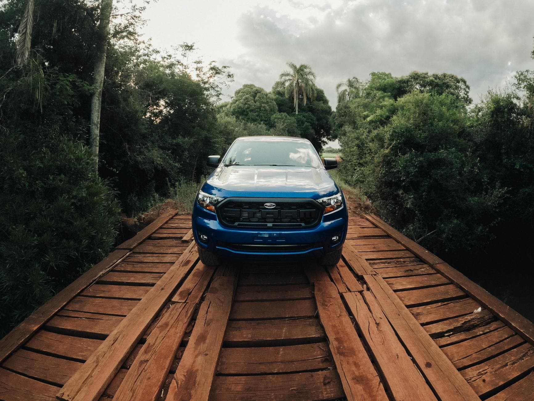 Blue SUV parked on a wooden bridge amidst lush greenery in Cruz Alta, Brazil.