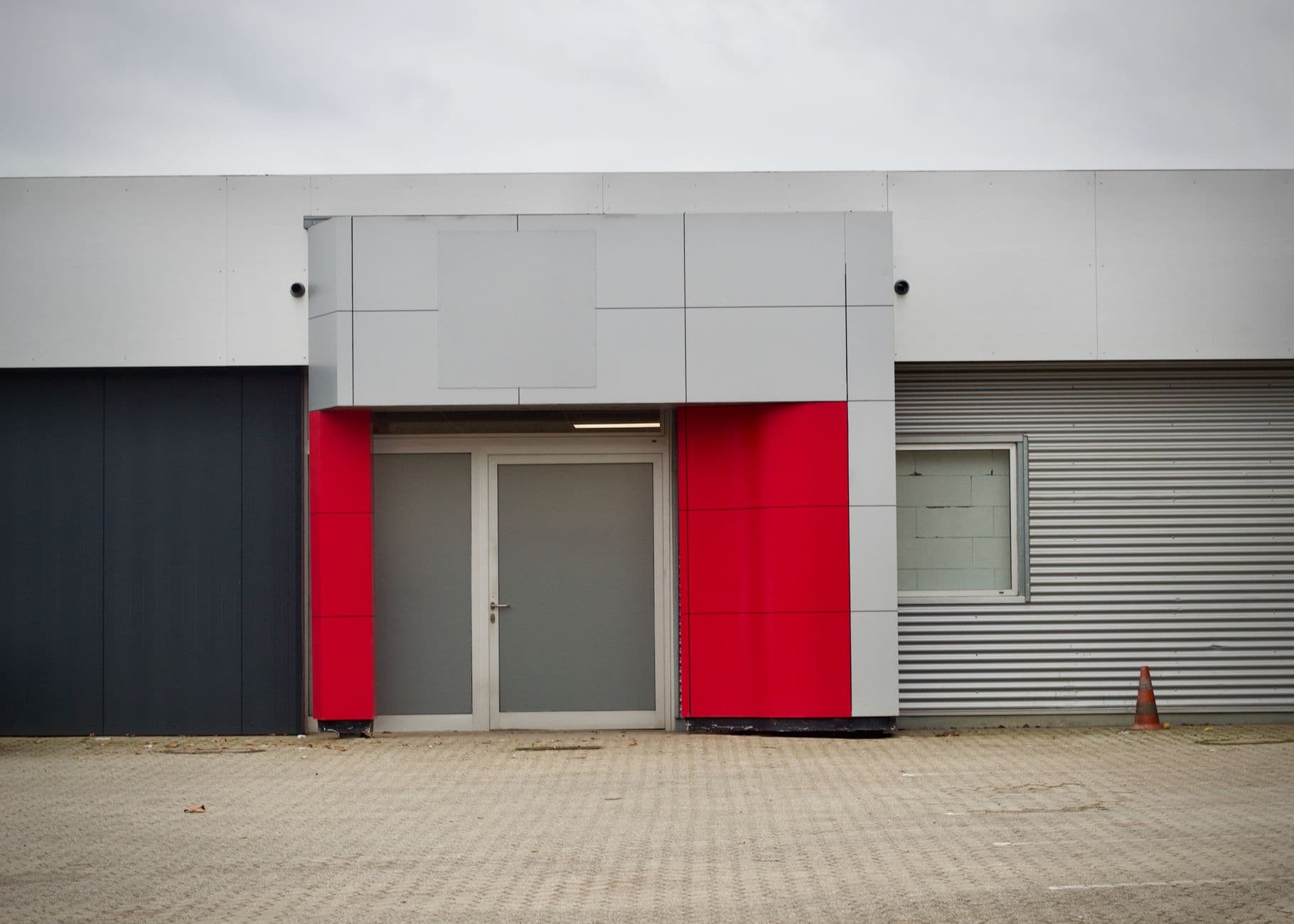Front view of a modern industrial building entrance with red accents and metal cladding.