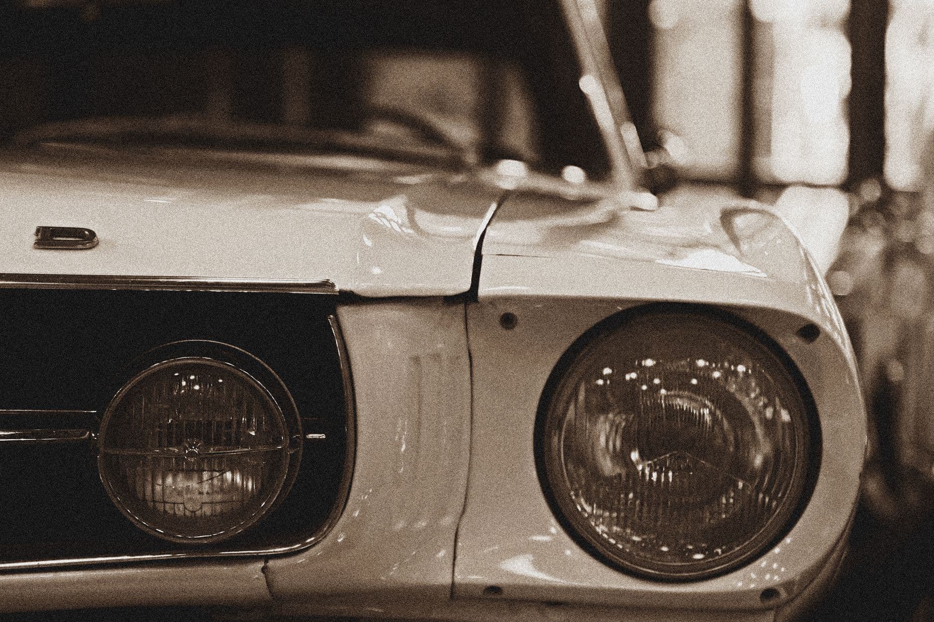 Sepia-toned close-up of a vintage car's front headlight and grille.