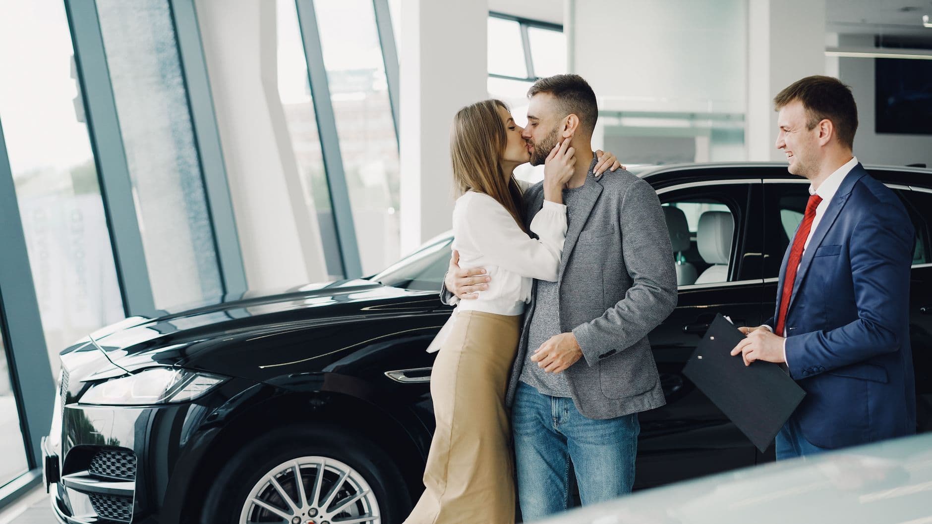Excited young couple kissing after purchasing a new car at a modern showroom.