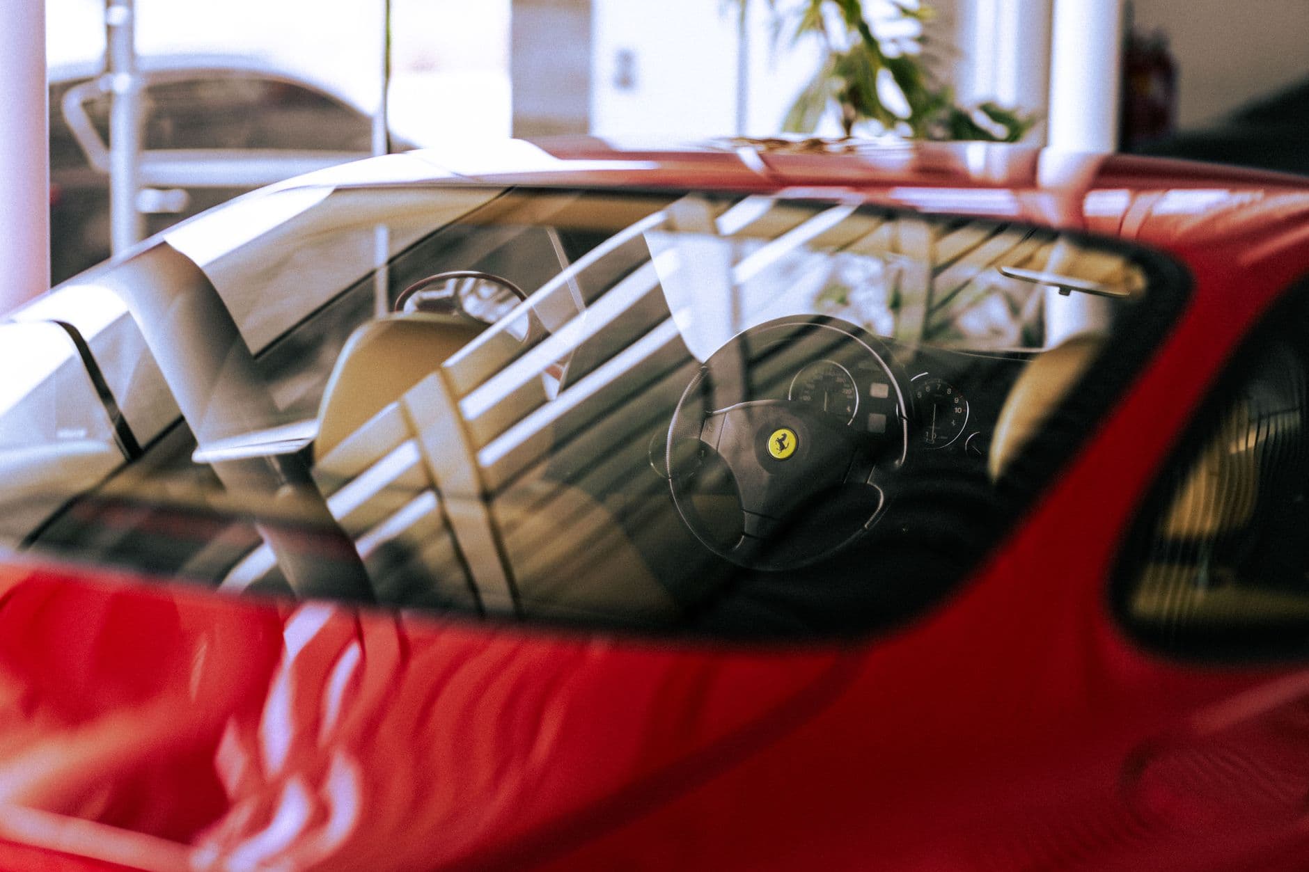 Close-up of a stylish red Ferrari interior with sunlight reflection in a showroom setting.
