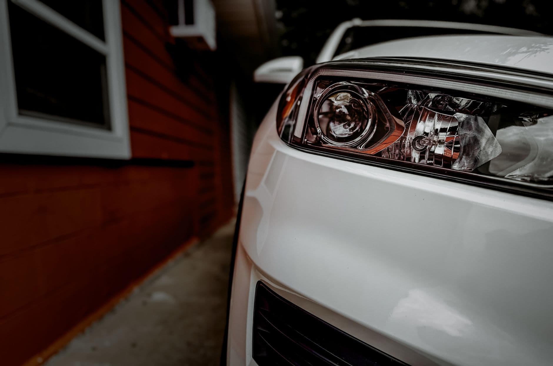Detailed focus on a white car's headlight with a red building background. Perfect for vehicle and architecture themes.