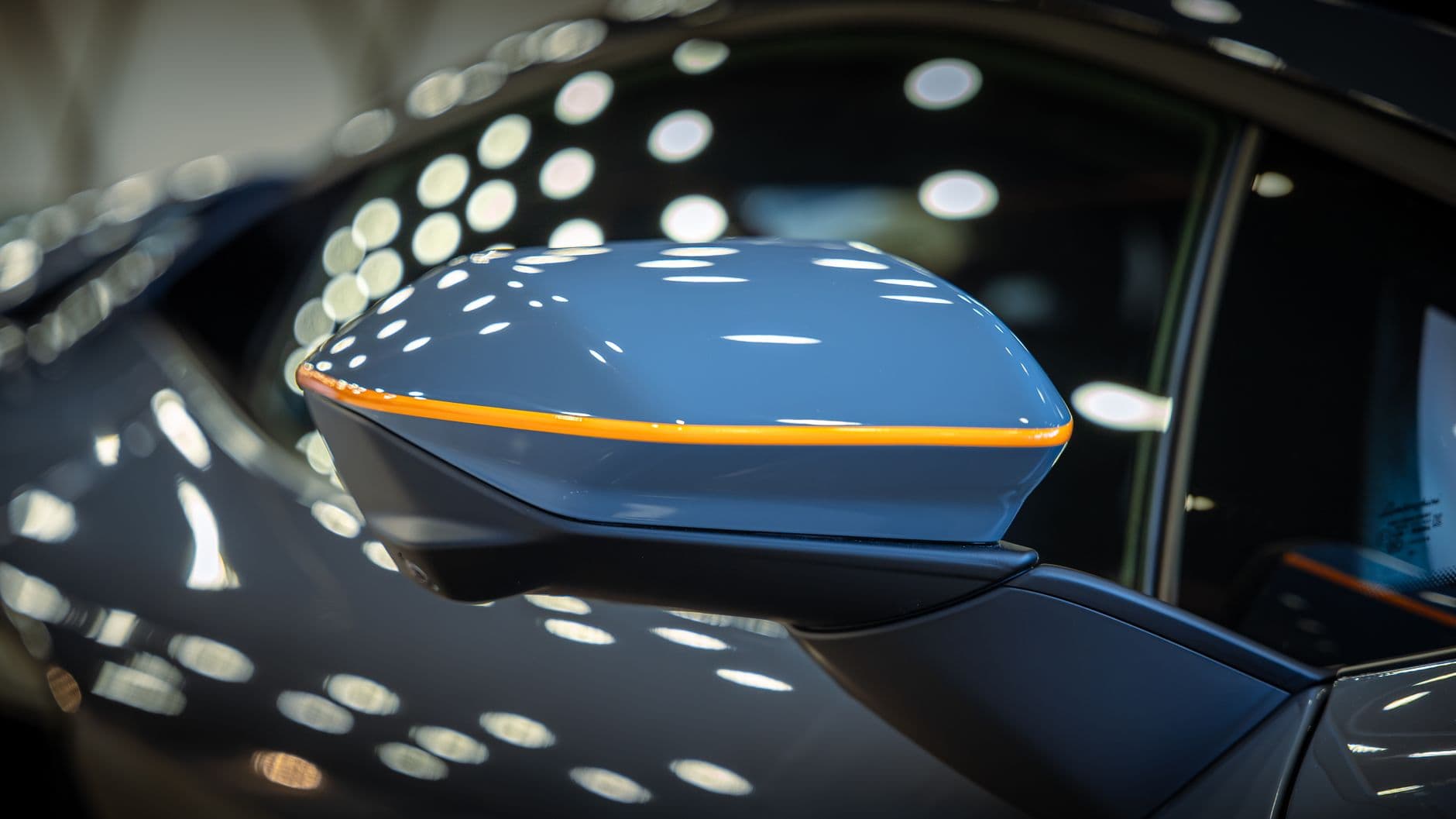 Detailed close-up of a stylish car side mirror reflecting ceiling lights in a showroom setting.
