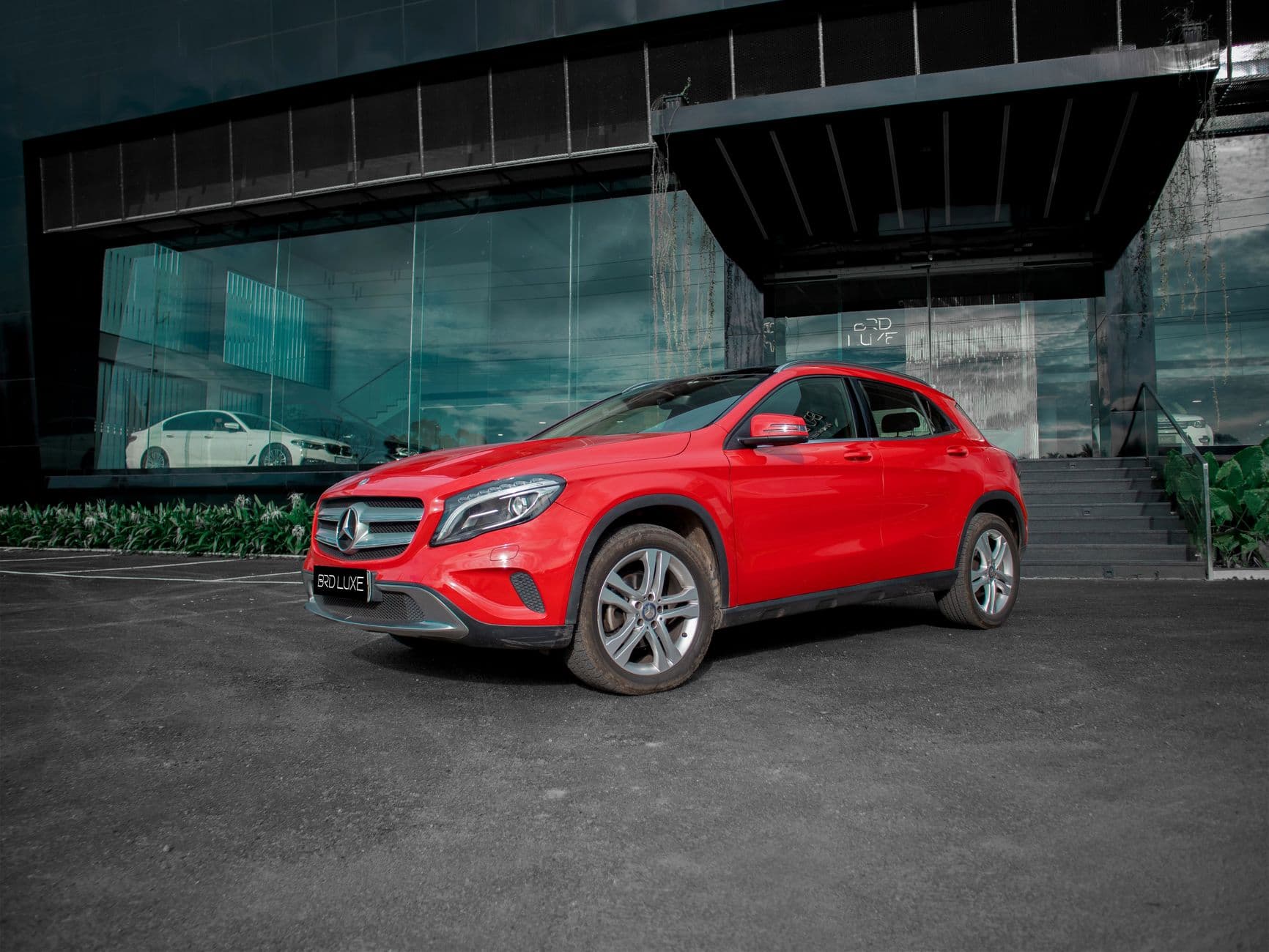 Vibrant red SUV, likely a Mercedes, parked in front of a modern glass building in an urban environment.