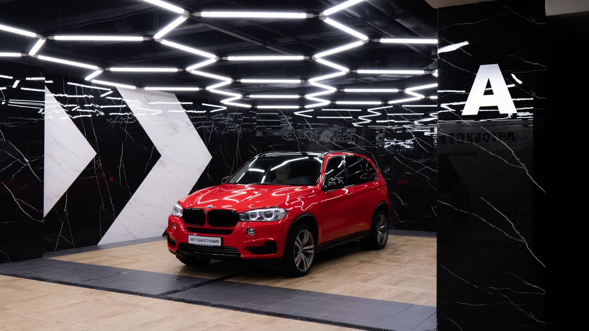 Red SUV showcased in a stylish showroom with geometric lighting and marble walls.