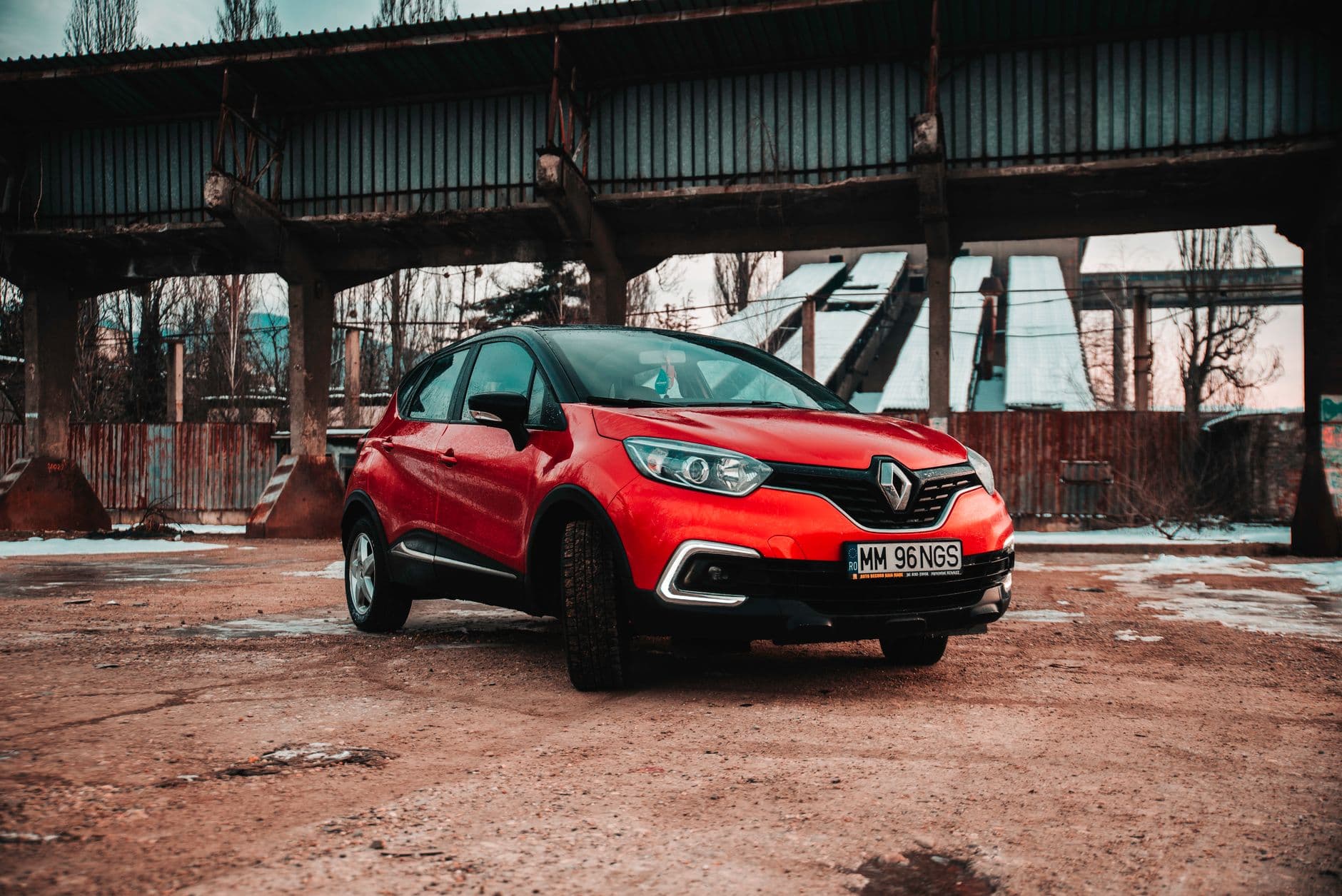 Striking red Renault Captur parked in a rugged industrial setting under a bridge.