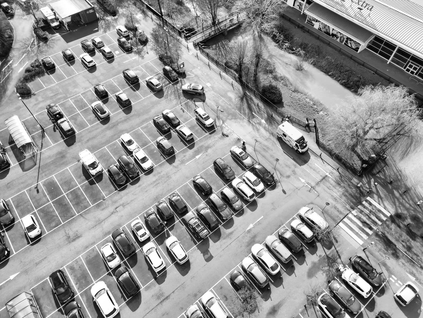 A high-angle, black and white aerial shot of a busy parking lot near a retail store.