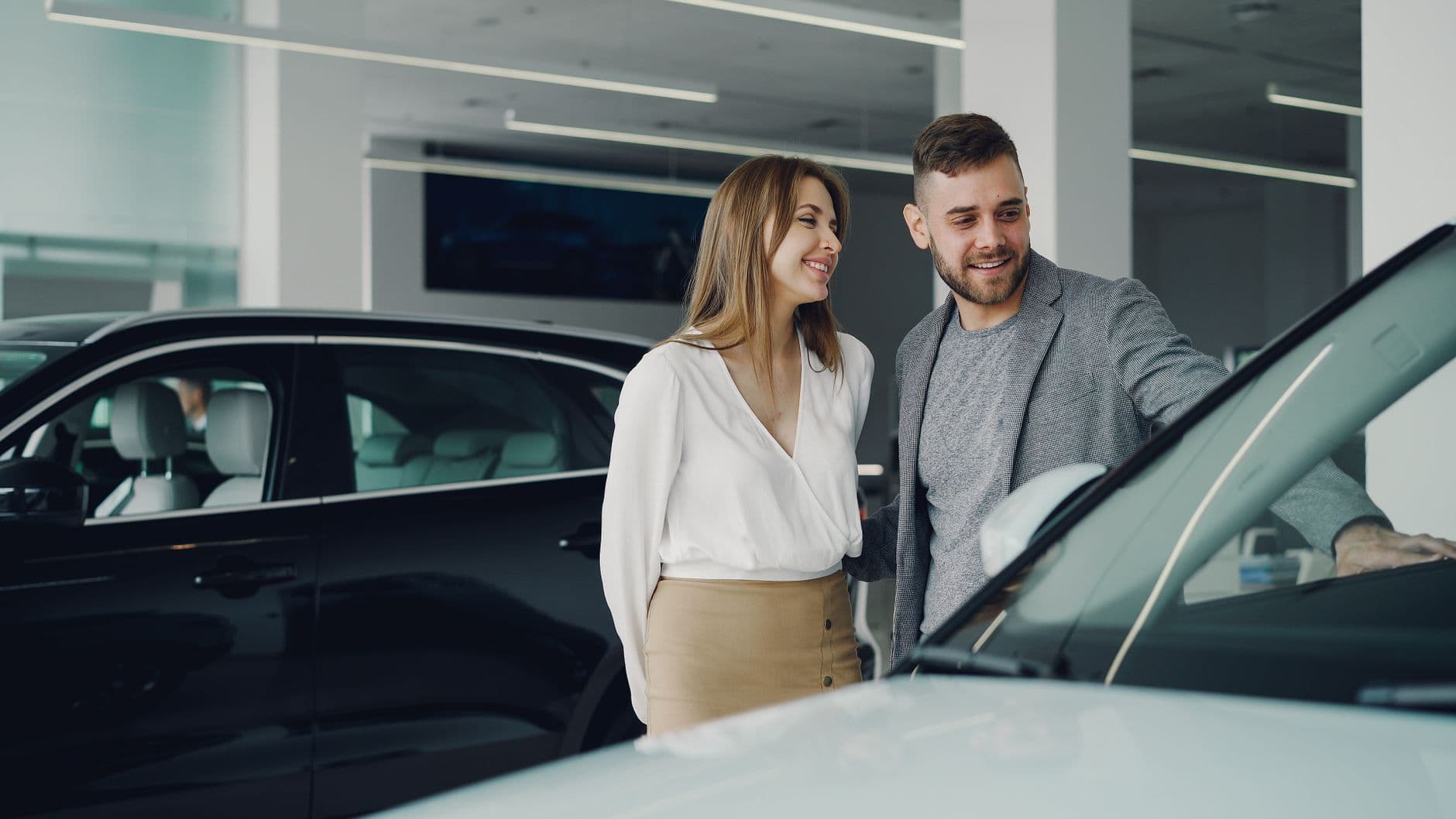 Smiling couple exploring cars at dealership, enjoying shopping experience.