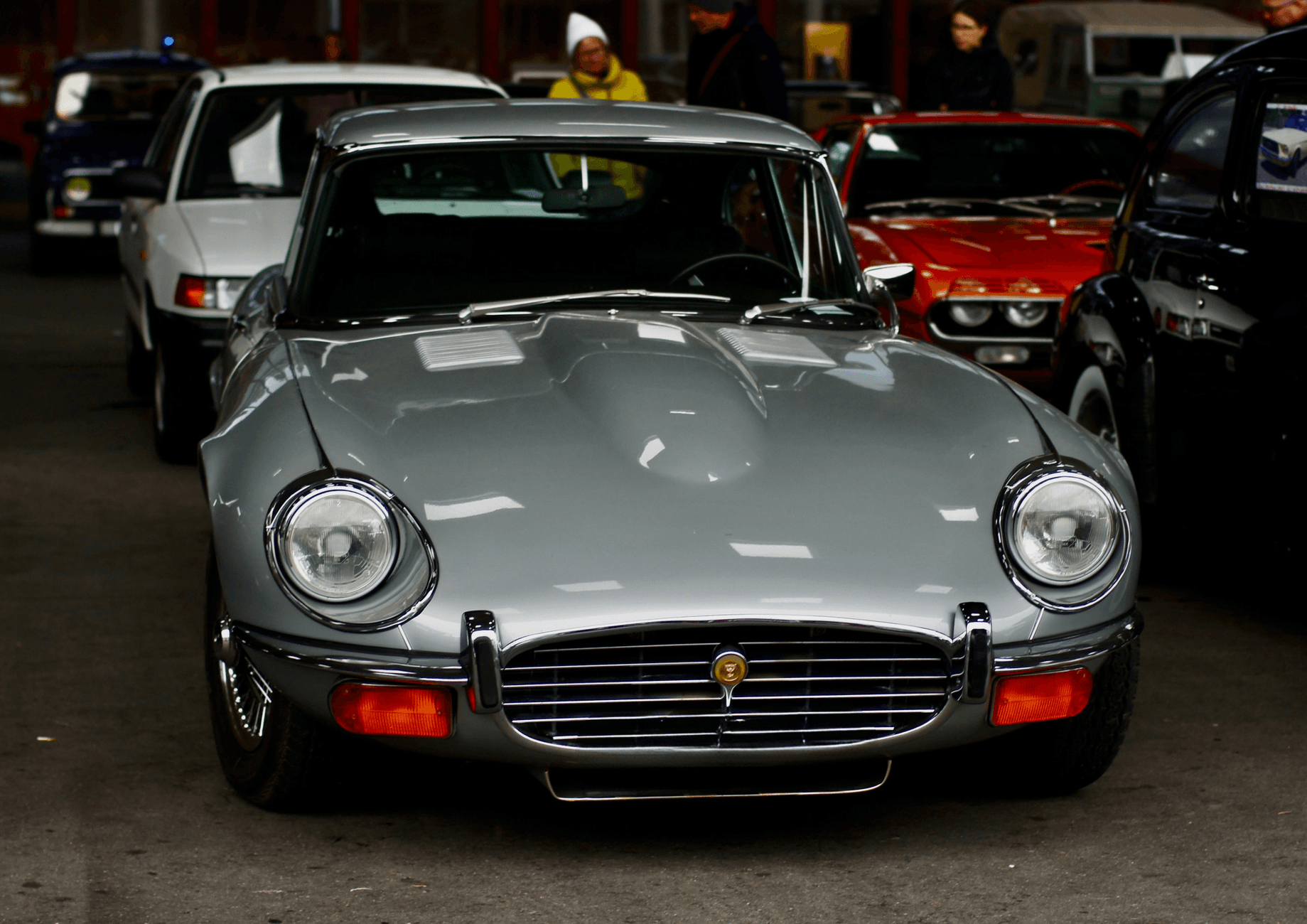 Front view of a classic Jaguar E-Type car showcased at an indoor auto show in Switzerland.