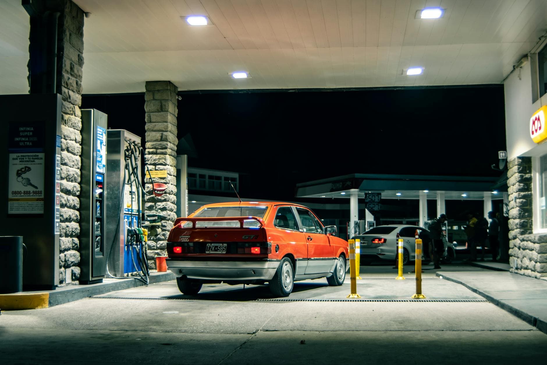 A classic red Volkswagen refuels at a rustic gas station in El Bolsón, Argentina.